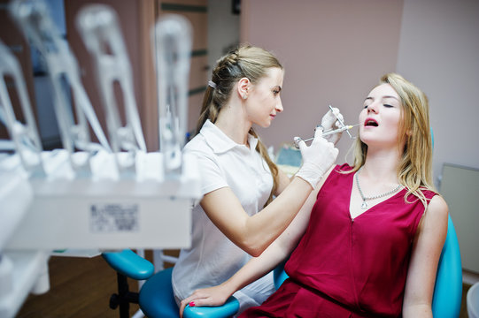 Attractive female orthodontist injecting anesthesia to her patient in a red-violet dress.