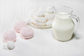 White and pink marshmallows and a jug of milk on a white wooden table. Beautiful light background. Food