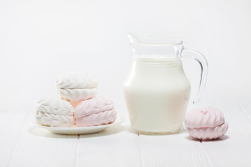 White and pink marshmallows and a jug of milk on a white wooden table. Beautiful light background. Food
