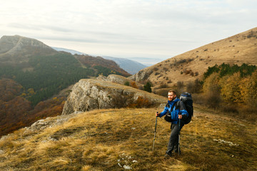 Obraz premium Redhead bearded hiker going up the trail path enjoying landscape. Backpacker man climbing a mountans with trekking poles. Beautiful autumn scenery