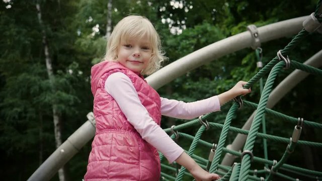 Positive blonde little girl playing on a children's playground. Slow motion. HD