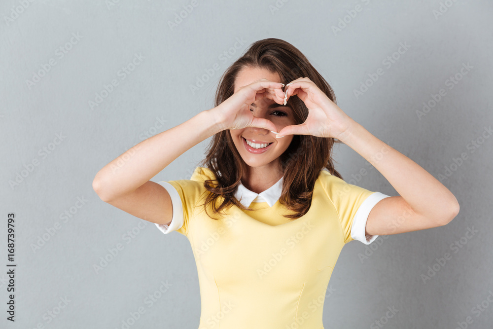 Wall mural pretty girl looking through heart gesture