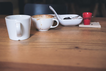 Many white coffee cups and dessert plate on wooden table in vintage cafe