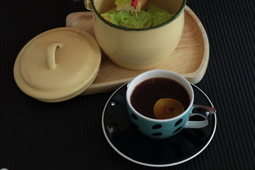 Lemon tea in blue glass with custard bread in a meat-colored jar placed on a black table for meals during the breaks.