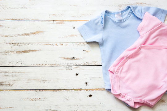 Pink And Blue Baby Romper On White Wooden Background

