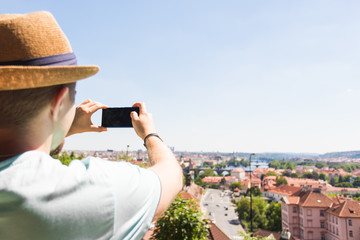 Fototapeta premium Back view of a young man tourist taking photo with smartphone in front of city