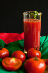 Glass and bottle of tomato juice with vegetables and green napkin on wooden background