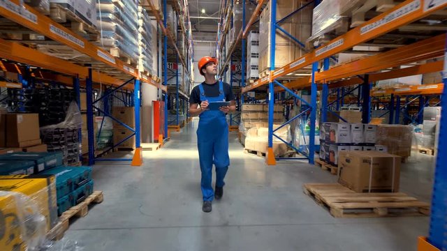 A worker in a uniform walks along a warehouse corridor.
