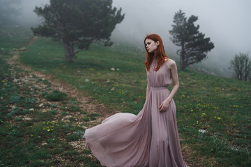 Beautiful young woman in a long dress in the mountains, fog