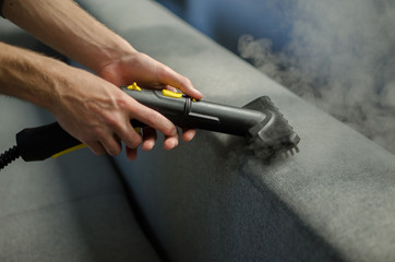 Hands cleaning a sofa with a steam cleaner