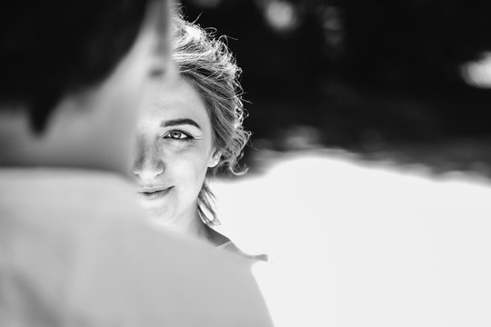 Beautiful bride in her wedding day looking at groom, fear and uncertainty in her eyes. outdoors. View from the back of a groom with copy space. Black and white image.