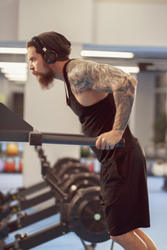 Strong tattooed black unlabeled tank t-shirt male athlete shows calisthenic moves Holding dip position on parallel bars