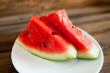 Ripe red watermelon on a wooden background. Slice of watermelon berries in a white plate