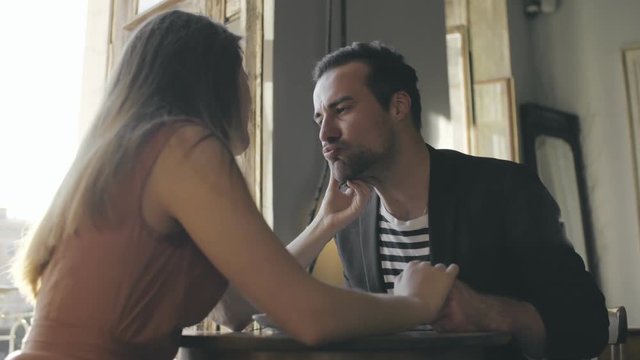 Girl in love stroking man on cheek at cafe table. Romantic date young couple