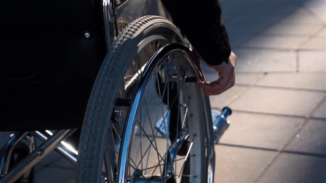 Rear view of a disabled man in wheelchair near business centre with focus on hand. He employee or businessman, moving to his work office. Slow motion shot 250 fps.