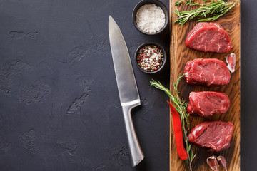 Filet mignon steaks and spices on wood at black background