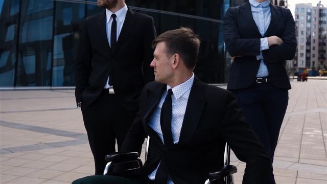 Epic shot paralysis handicap health concept. Disabled male with disabled legs sitting on wheelchair and colleagues back. Neutral and sad emotion. Super slow motion high speed camera.