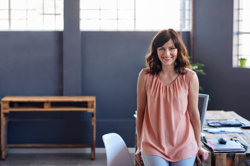 Smiling young businesswoman leaning on a desk in an office  