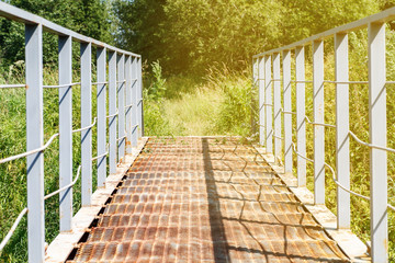 Old metal bridge among high grass in warm sunny summer day