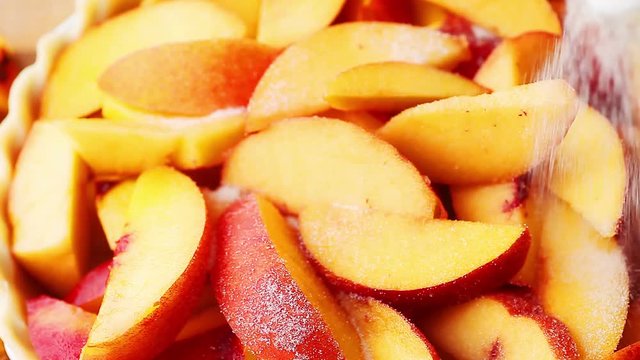Sprinkling spice and sugar on peaches in a pie crust