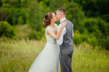 Young couple in love, groom and bride in wedding dress at the nature. The groom kisses his bride in the nose. Wedding. Wedding day. Bridal bouquet.