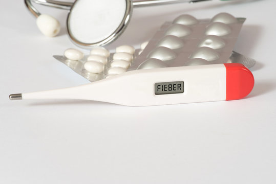 Ein Stethoskop, Tabletten und ein digitaler Thermometer mit dem Wort Fieber im Display