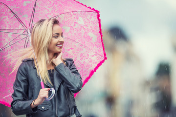 Attractive young woman with pink  umbrella in the rain and strong wind. Girl with umbrella in...