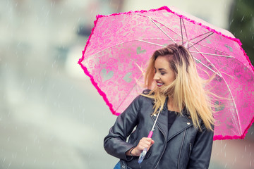 Attractive young woman with pink  umbrella in the rain and strong wind. Girl with umbrella in autumn weather