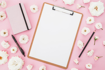 White roses flowers with clipboard, notebook and pen on pink background. Flat lay, top view. Female business background.