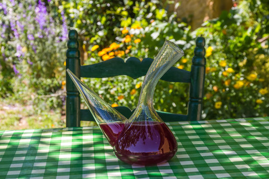 Recipiente para beber Vino tipico de Espa&ntilde;a ( Porron ) con sangria encima de una  mesa a la sombra de verano en el jardin o patio de la casa, con una silla