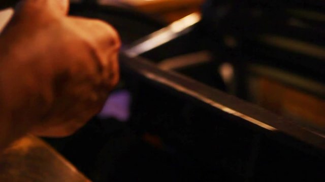 Printer checks the quality of his work while his antique press continues to run