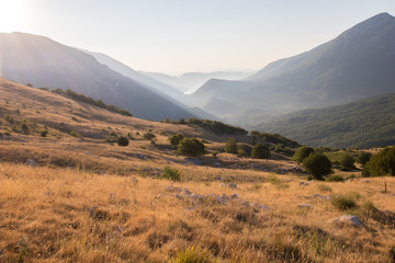 Green mountains with yellow grass fields and lake in the background. Barrea lake seen from the Marsicano mountain in Abruzzo in early morning with sun