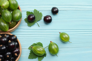 black currant in wooden bowl with gooseberry on blue wooden background. top view with copy space