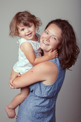 Group portrait of young middle aged white Caucasian mother and daughter baby girl hugging smiling laughing. Family studio session photo on plain light background. Happy lifestyle childhood concept.