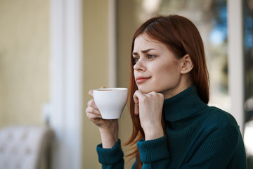 Beautiful young woman drinks coffee in a cafe on the street