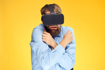 A young guy with a beard on a yellow background in virtual reality glasses