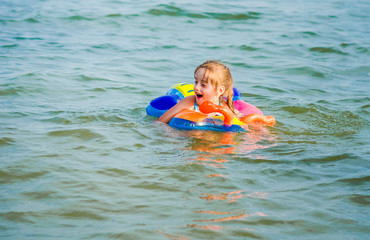 Six-year girl swims in the sea sat on the rubber ring, swimming and happily smiles.