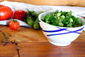 Salad of tomatoes and cucumbers in a bowl and vegetables on a wooden table