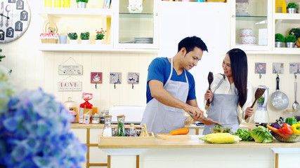 Young asian couple are teasing while cooking in the kitchen.