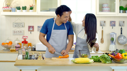 Young asian couple are teasing while cooking in the kitchen.