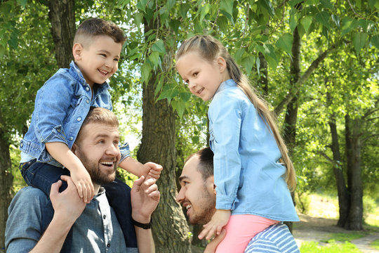 Smiling gay couple with children in park