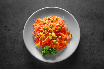 Delicious spicy carrot spaghetti with peas, pepper and parsley on table