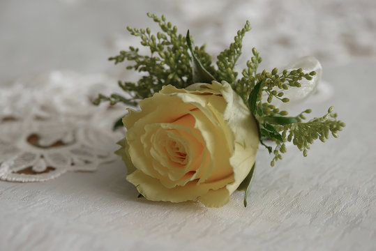 Wedding accessories: fresh yellow rose small bouquet for buttonhole used for groom and wedding guests positioned on a white cloth, in natural light