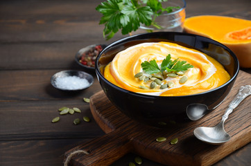 Pumpkin cream soup with cream and pumpkin seeds on wooden background, selective focus, horizontal