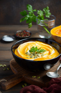 Pumpkin cream soup with cream and pumpkin seeds on wooden background, selective focus, vertical