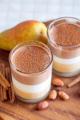 Delicate three-layer mousse with ricotta, chocolate and caramel. Glass glasses, cinnamon sticks, almonds and pears on a dark wooden board.
