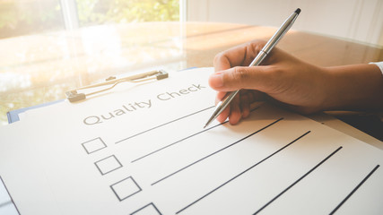 Close- up hand holding pen on quality check paper and the format for filling in information in business concept,vintage style and softtone.