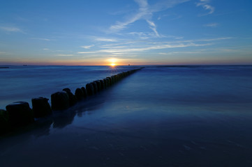 Fototapeta na wymiar Poland, Baltic. Sunset over the sea. Breakwater on the smooth surface of the sea.