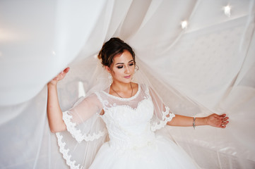 Portrait of a stunning bride posing with curtains in her room on a wedding day.