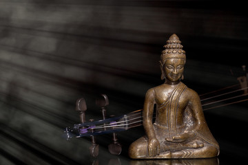 Music therapy. Spiritual, New Age, and religious music represented by bronze buddha meditating with contemporary violin in divine beam of light.